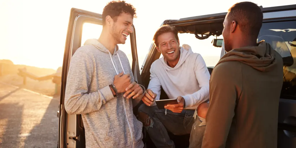 Three male friends laughing with each other on a road trip