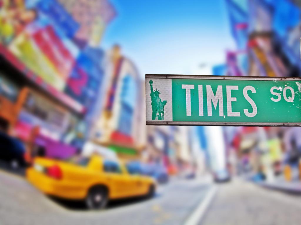 Close up view of Times Square sign with yellow cab and bright lights of Times Square in the background