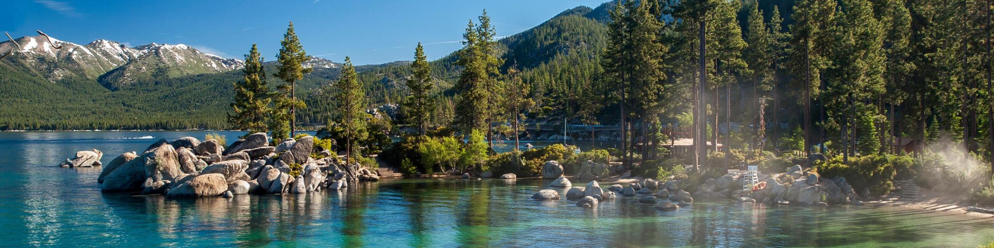 Clear emerald water with rocks, pine trees and mountains at Sand Harbor SP, Lake Tahoe, Nevada