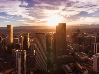 Panoramic aerial shot of the Denver skyline in Colorado at dusk, with wispy clouds drifting across the setting sun