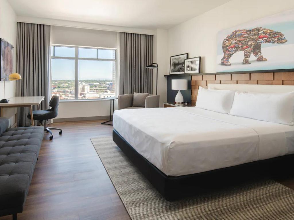King Concierge modern bedroom at The Bidwell Marriott Portland, with large windows and city views, desk, sofa and large bed, with statement bear print above headboard