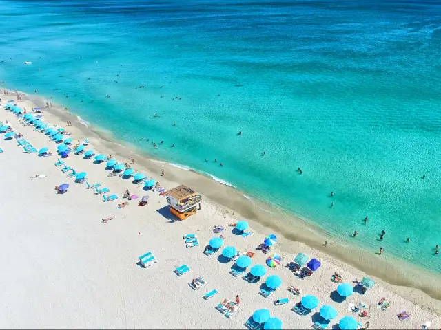 Aerial view of white sand and turquoise sea with a few sunbathers and swimmers just visible