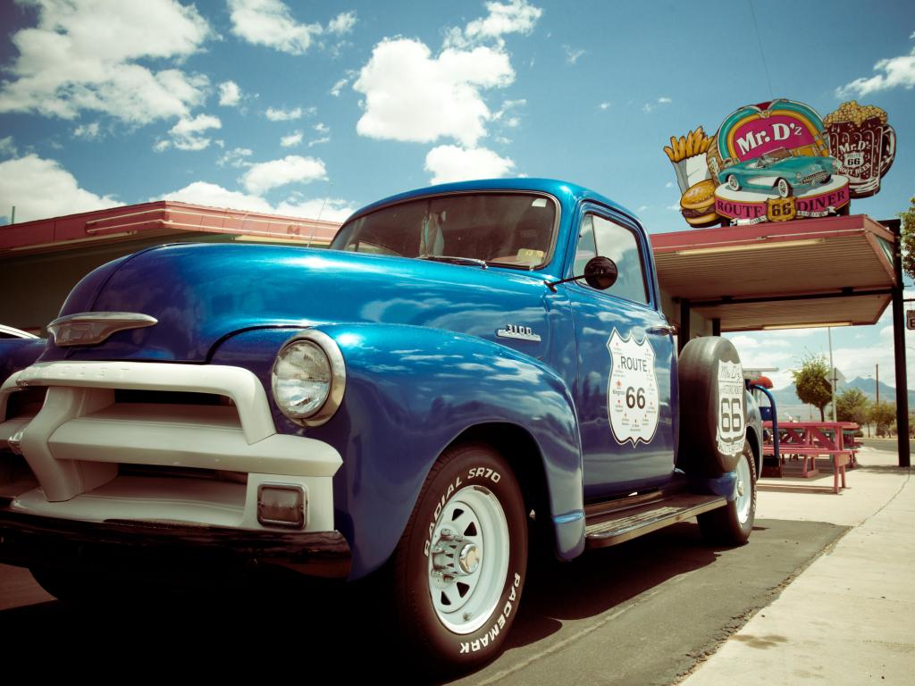 Roadside Route 66 attraction with old van and a fast food restaurant in the background