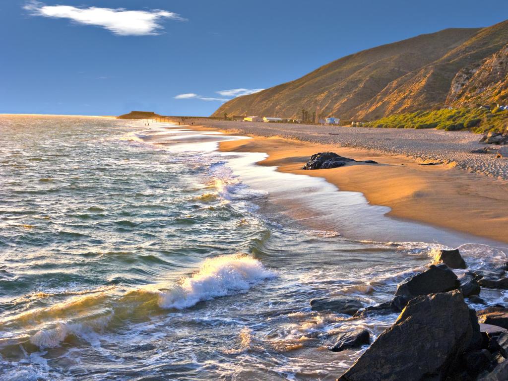 Late afternoon at the beach in Oxnard, California, with the sun casting an orange glow on the sand and rocks