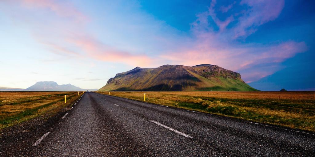 Looking down a road with a mountain to one side during a colourful sunset, in Iceland