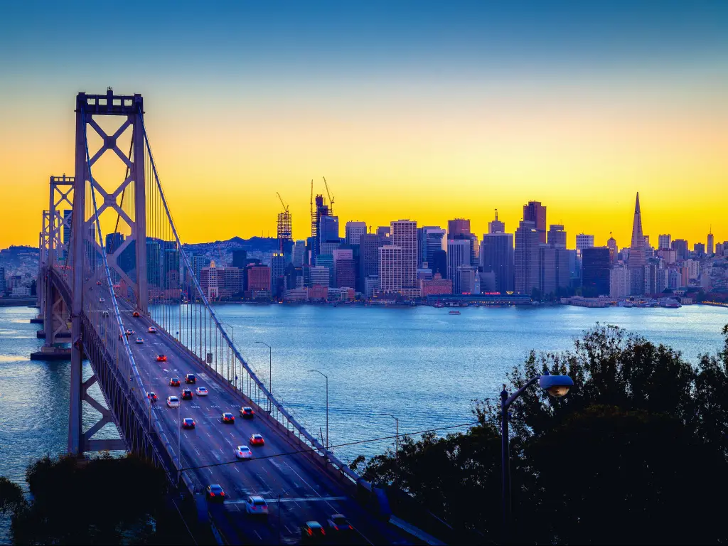 A beautiful twilight golden sunset glow of summer illuminating the skyline of San Francisco and a panoramic view of the famous Oakland Bay Bridge with cars driving along the bridge (Interstate 80)