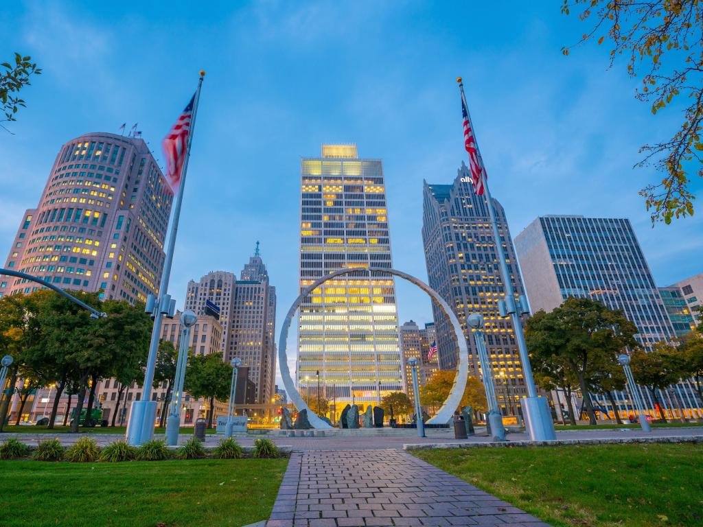 Highrise buildings with circular statue and two flagpoles flying the US flag in the foreground