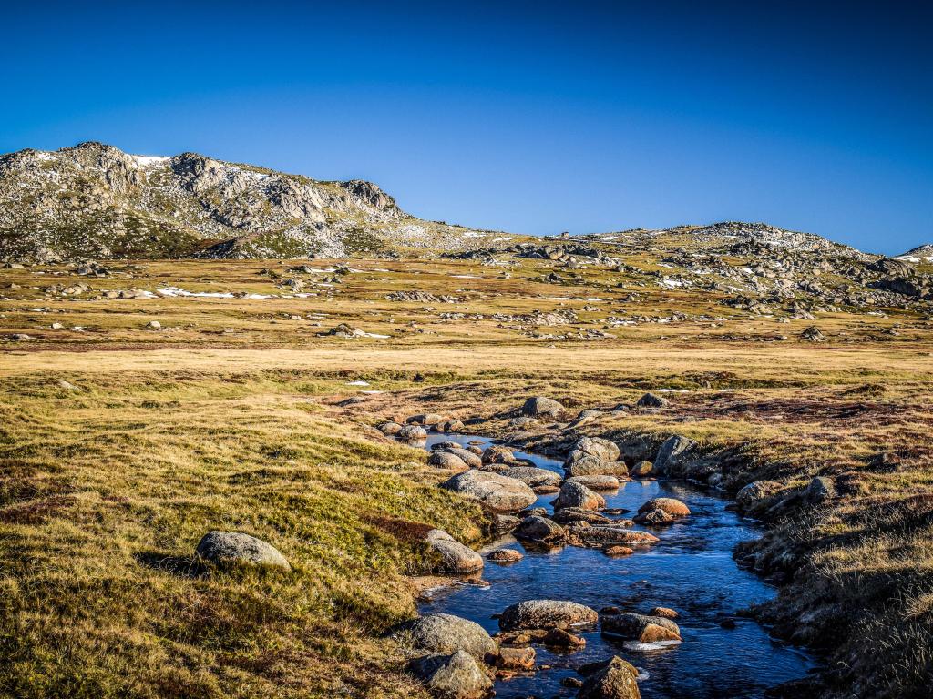 Kosciuszko National Park, Australia with a stream in the foreground leading towards snow capped mountains in the background.