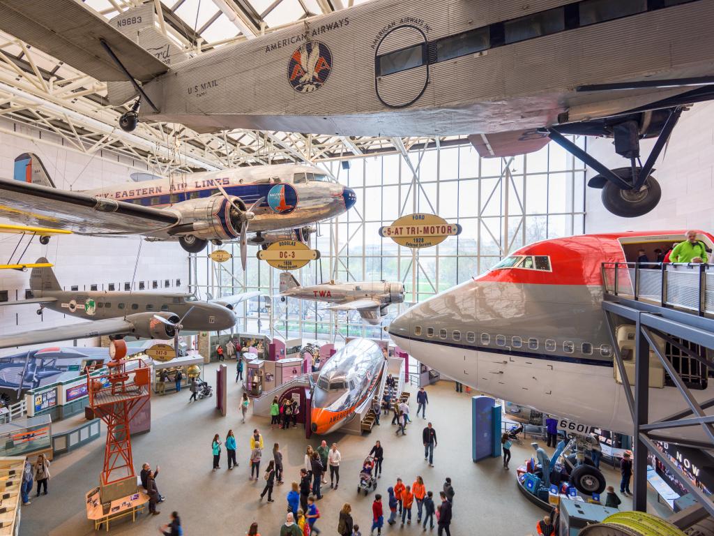 Visitors enjoying the museum, with old planes hanging from the ceiling