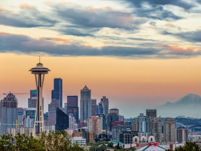 Seattle Skyline at sunset. The photo is taken on a slightly cloudy day and the clouds reflect the dramatic colors of the sunset. Space Needle can be seen.
