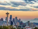 Seattle Skyline at sunset. The photo is taken on a slightly cloudy day and the clouds reflect the dramatic colors of the sunset. Space Needle can be seen.