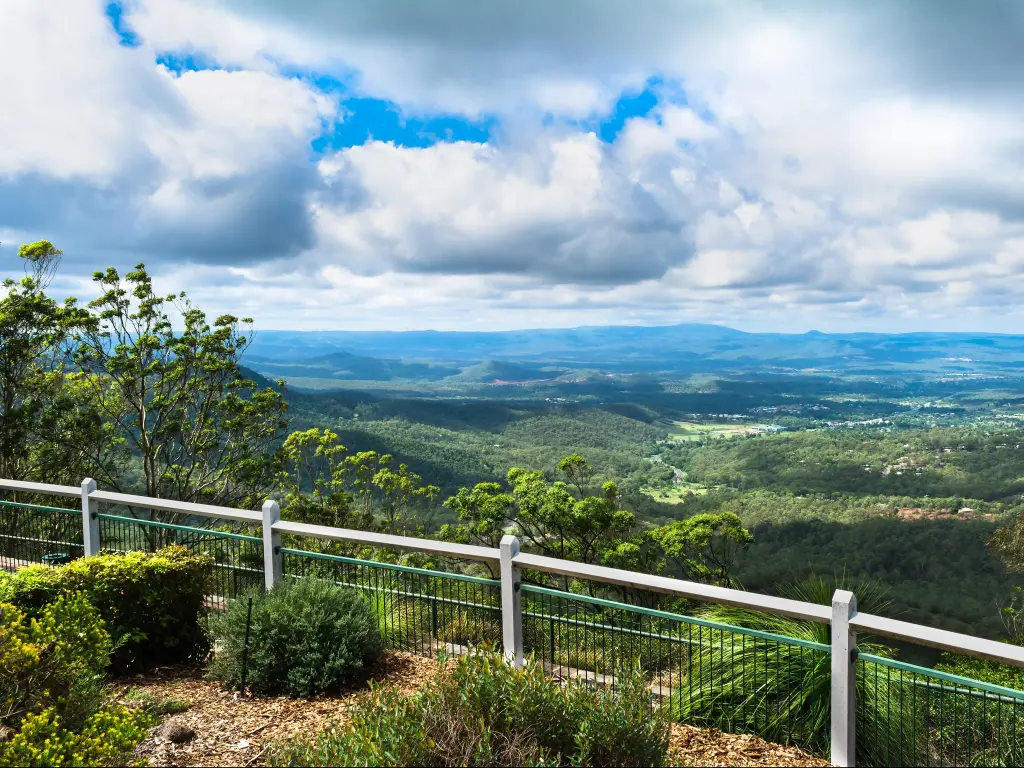 Toowoomba, Australia with a fence in the foreground overlooking panoramic views of flat lands and mountains below on a sunny day.