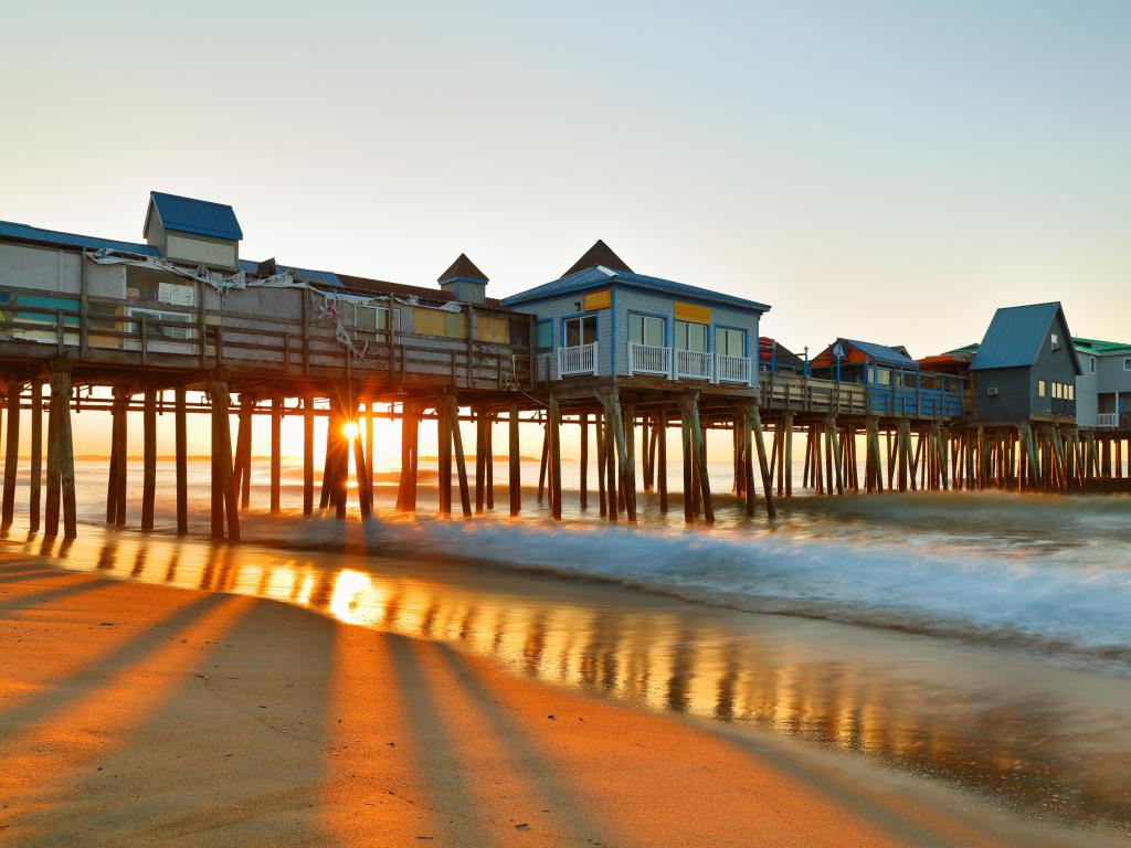 Old Orchard Beach, Maine USA with the iconic pier taken at sunrise, with the beach in the foreground and a calm sea.