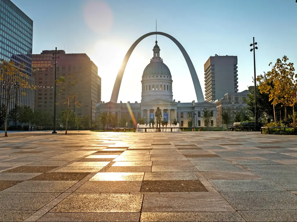 Taken from a low vantage point, a modern arch sweeps around the dome of a historic white building with a fountain in front