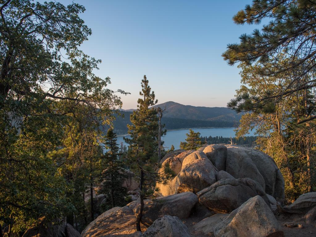 Big Bear Lake, California, USA with large rocks in the foreground and trees and the lake and mountains beyond taken at dawn.
