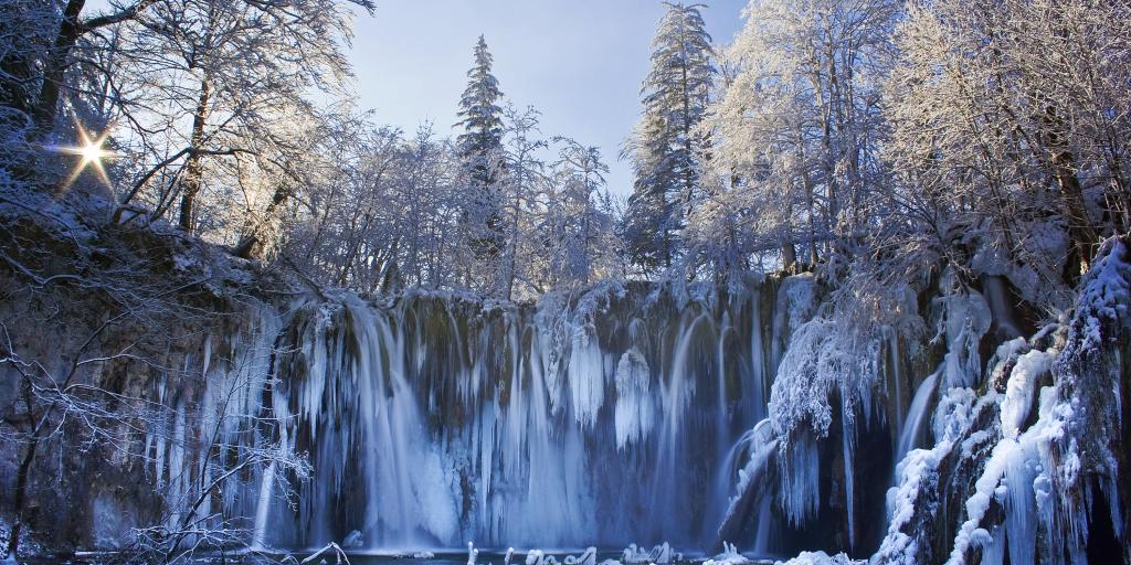 A frozen waterfall in Plitvice National Park surrounded by snow coated trees