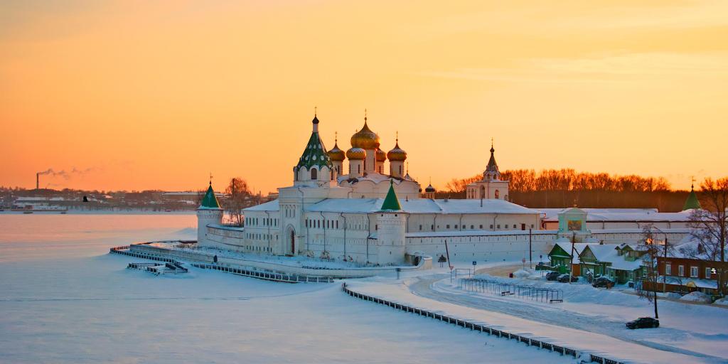 The Ipatiev Monastery in Kostroma, Russia, shown in winter at sunset, with the lake in front frozen and the gold domes visible
