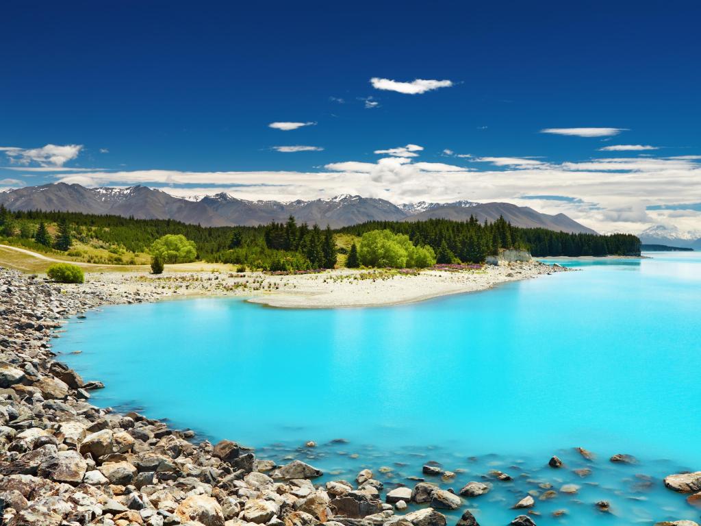 Piercing light blue waters against the rocks with mountains in the background at lake Pukaki