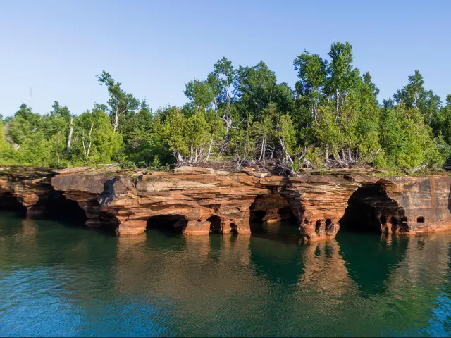 Apostle Islands National Lakeshore, Wisconsin, USA with a view of the rocky shores of the Apostle Islands National Lakeshore with water in the foreground and blue sky.