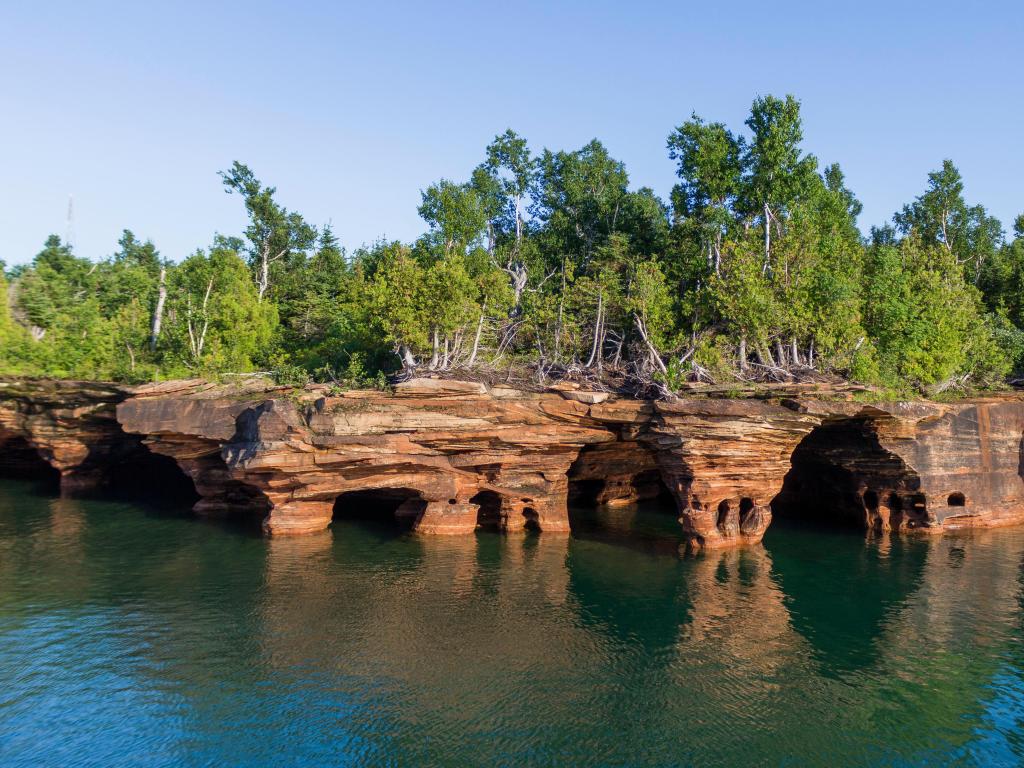 Apostle Islands National Lakeshore, Wisconsin, USA with a view of the rocky shores of the Apostle Islands National Lakeshore with water in the foreground and blue sky.