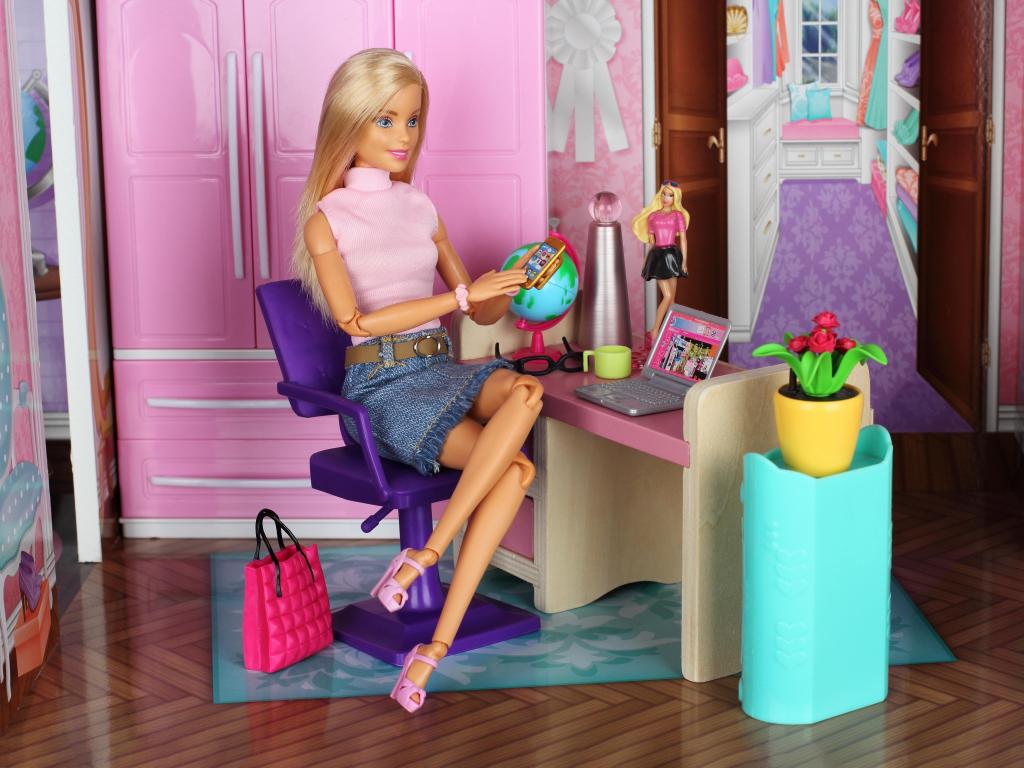 A Barbie in a doll house, sitting at the toy office space