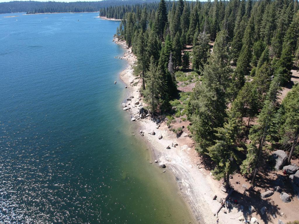 Aerial photo of Shaver Lake, California, with its turquoise waters lapping against white rock and a dense forest of pine trees 
