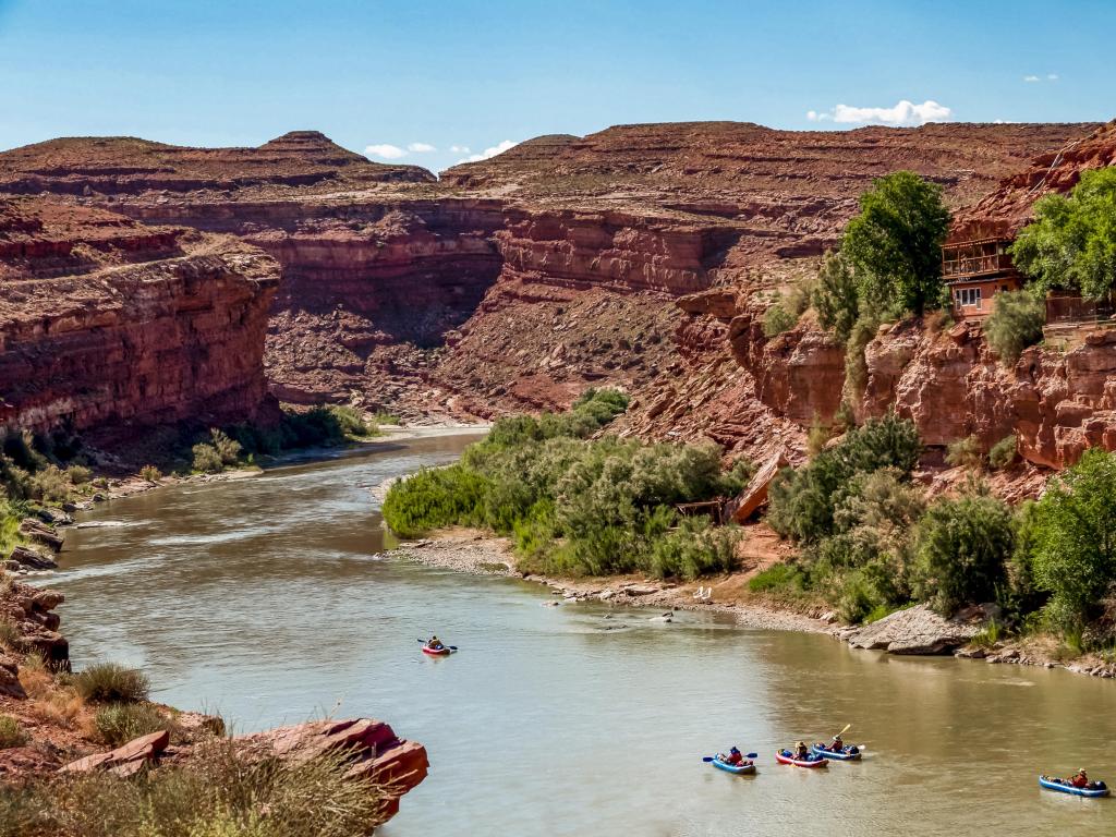 San Juan River, Utah, USA with people canoeing on the river near Goosenecks State Park on a sunny day, cliffs and trees surrounding the water.