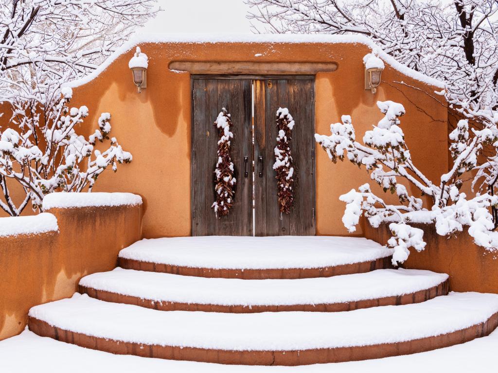  Snow-draped adobe wall featuring rustic wooden doors and chili ristras 