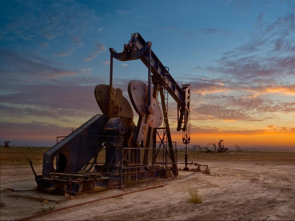 San Joaquin Valley, California, USA with an oil well and pump jack in the foreground taken at sunset.