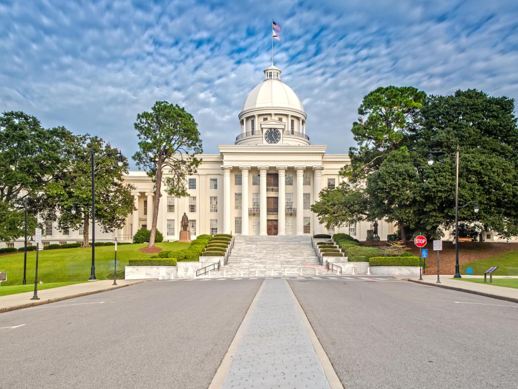 Alabama State Capitol, Montgomery with a road in the foreground leading to the historic building, tall trees either side of the road on a cloudy day.