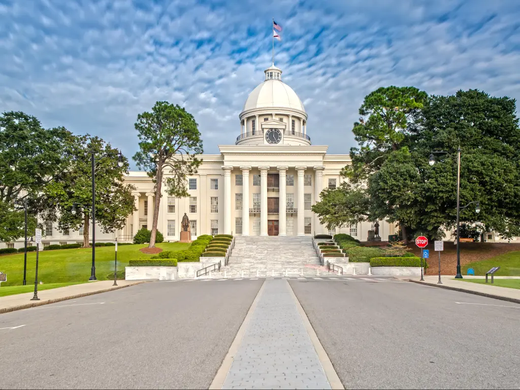 Alabama State Capitol, Montgomery with a road in the foreground leading to the historic building, tall trees either side of the road on a cloudy day.
