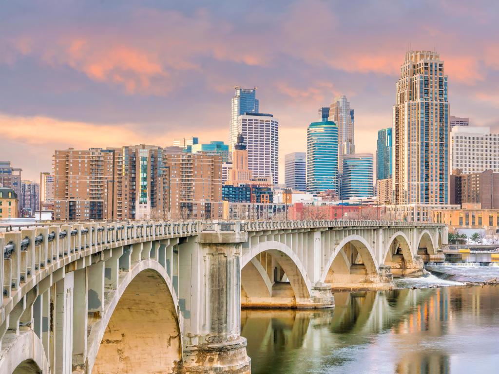 Minneapolis, Minnesota, USA with a view of the downtown skyline at sunset with the bridge in the foreground and city in the background.