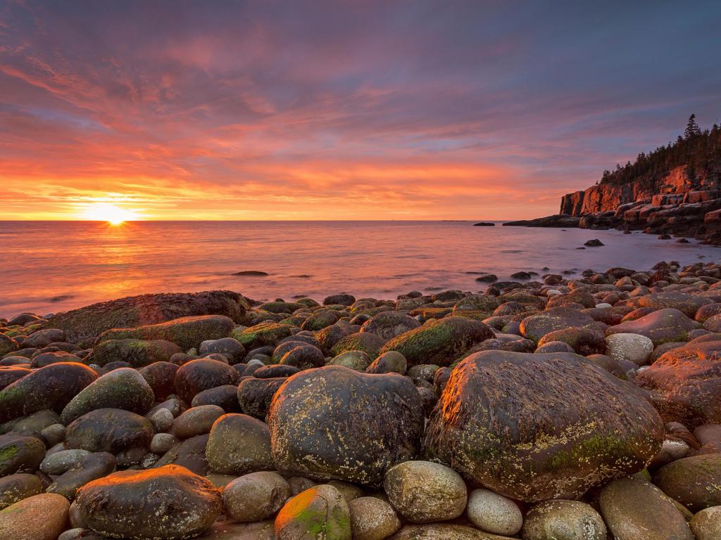 Sunrise at Acadia National Park with big rocks in the foreground and the ocean reaching into the horizon