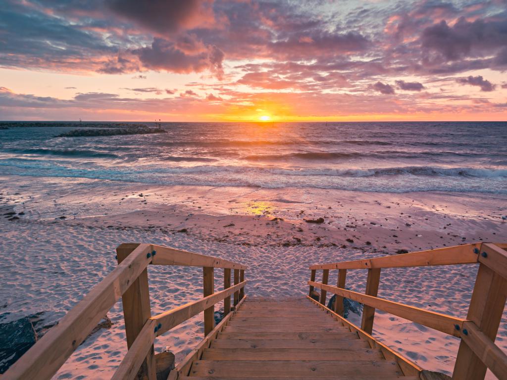 Sunset over the ocean with wooden steps leading down to a sandy beach in the foreground