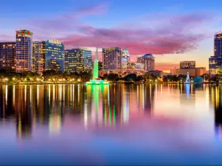 Orlando, Florida, USA downtown city skyline from Eola Park at night with the city skyline reflecting in the water in the foreground.