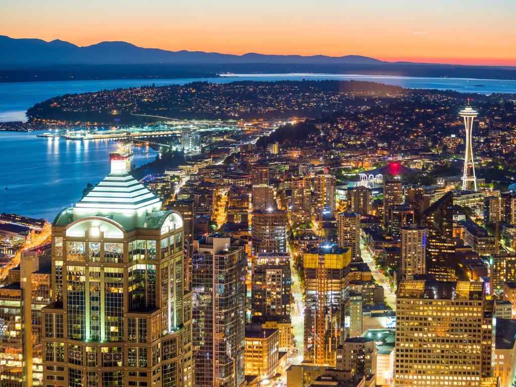 View of highrise Seattle buildings lit up at night with river running behind and silhouette of far bank