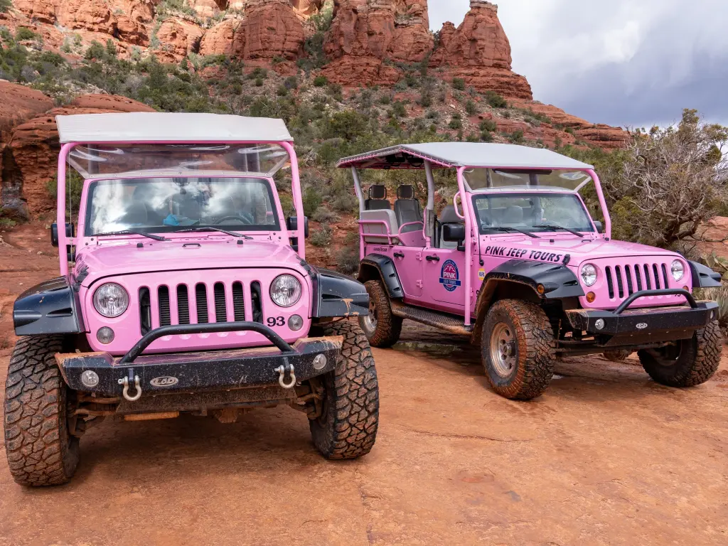 Two pink Jeeps parked on rugged red rocks, with red cliffs in the background