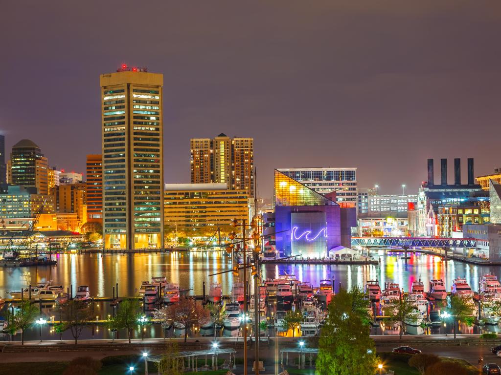 Baltimore, Maryland, USA with a view of downtown Baltimore at night, with boats in the harbor in the foreground.