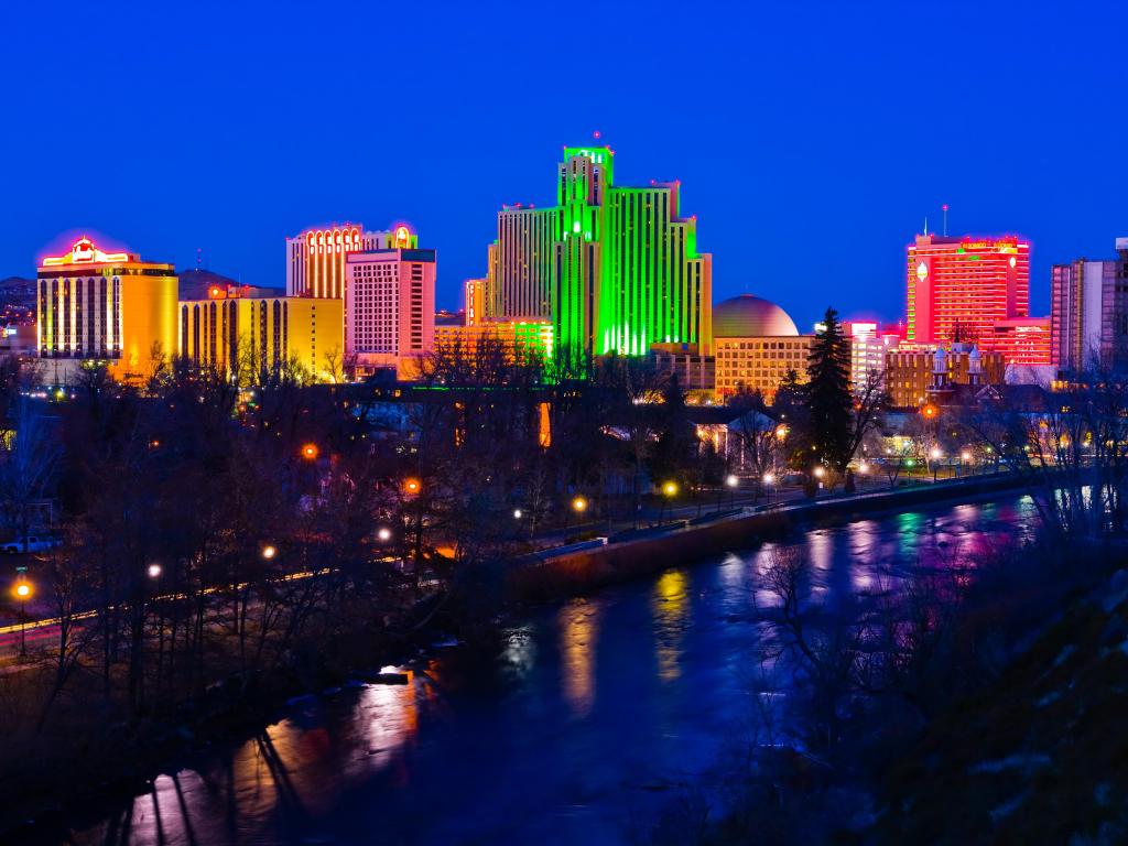 The colorful city of Reno at night. The buildings are illuminated in neon-colored lights which reflect on the water.