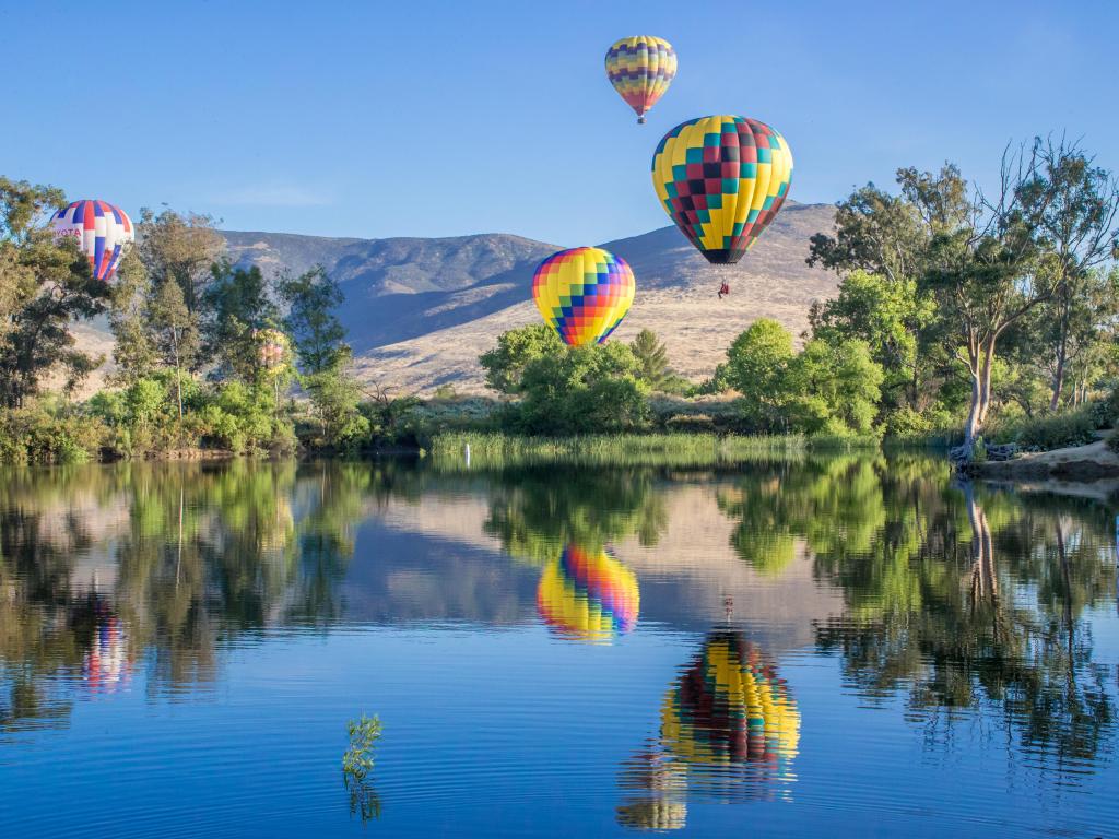 Mountains in the background, with colourful hot air balloons in the air reflecting in the lake.