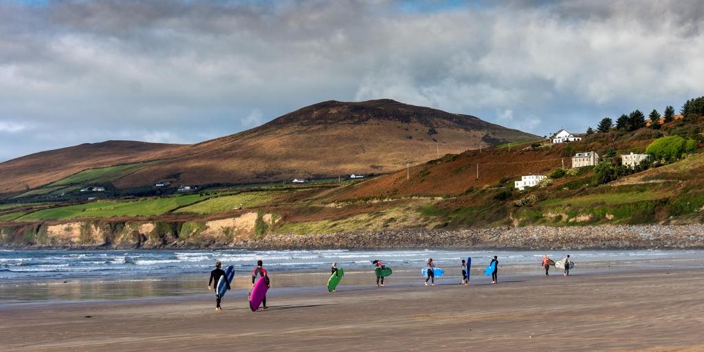 Surfers walking down Inch Beach in Ireland carrying their boards