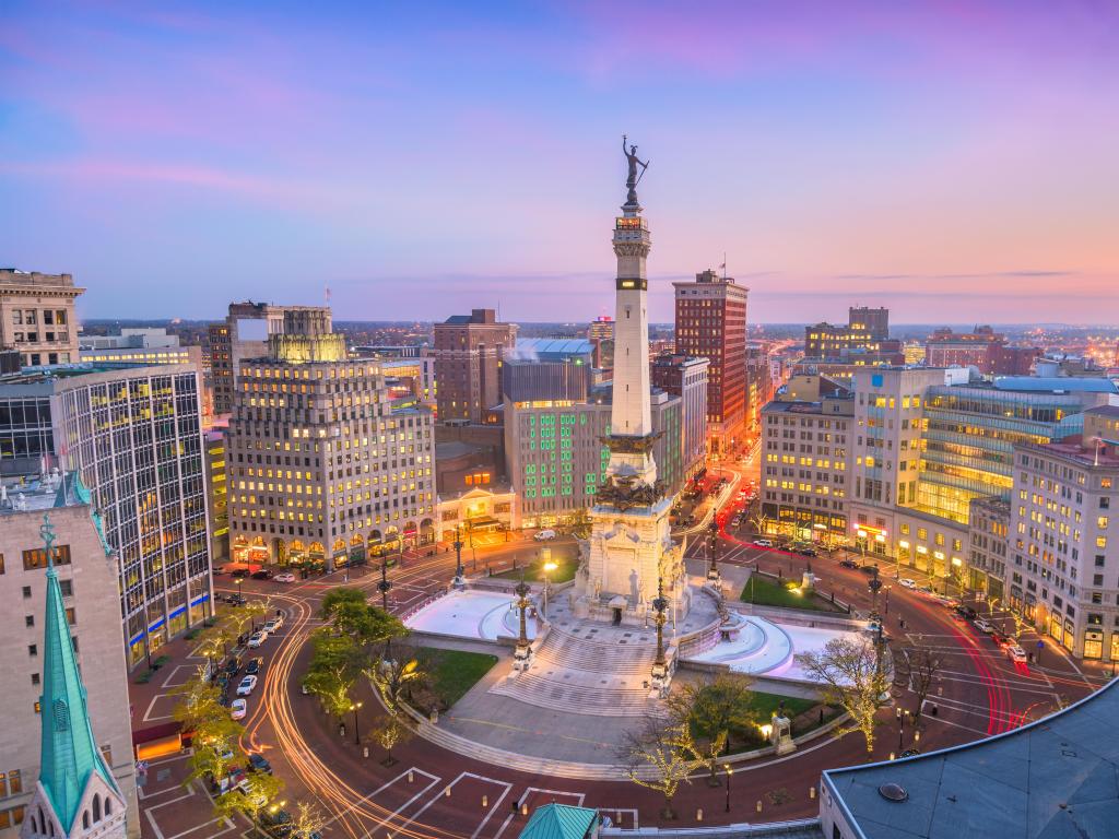 Indianapolis city skyline at sunset with a purple hued sky behind and Soliders' and Sailors' Monument below