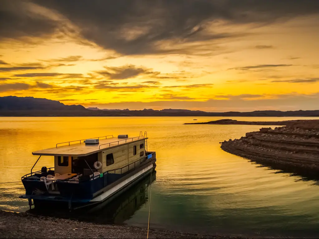 Lake Mead National Recreation Area, Nevada, USA with a houseboat moored to the muddy shores taken at dusk with a dramatic and colorful cloudy sky.
