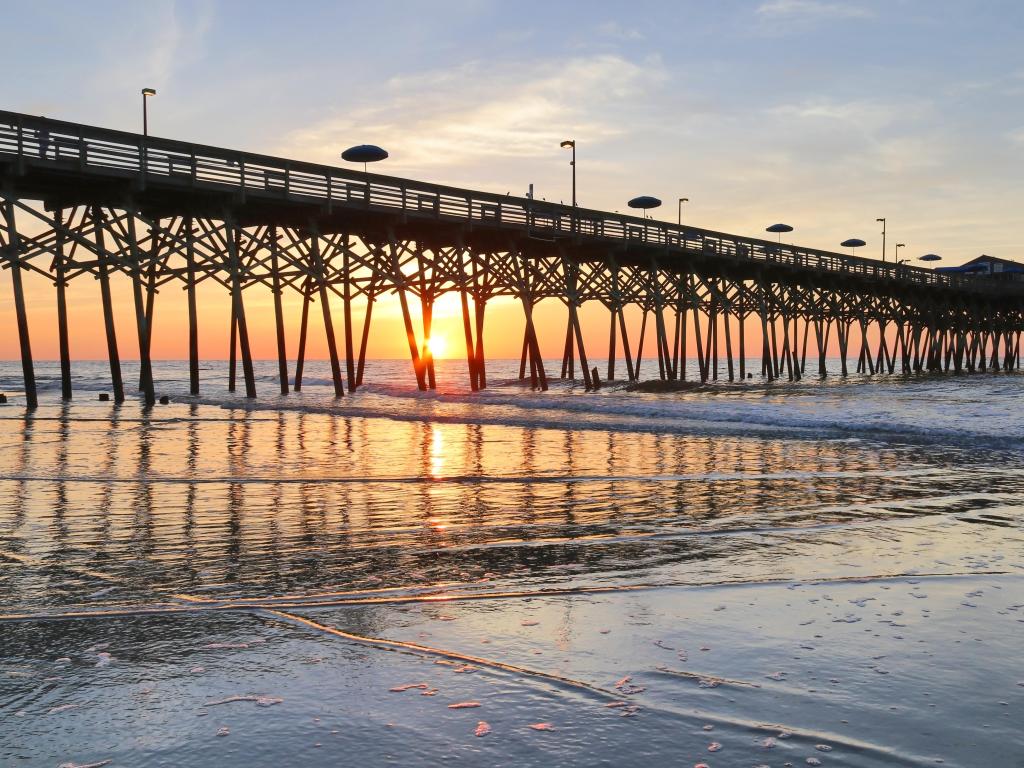 Early morning at the Atlantic Ocean beach. Beautiful marine landscape with sun rising over calm Atlantic Ocean beach with wooden pier. South Carolina, Myrtle Beach area, USA.