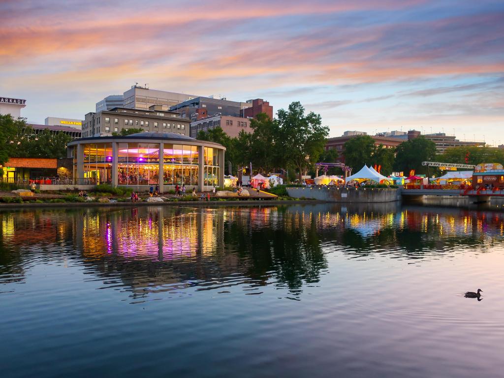 Spokane, Washington, USA with a view of the Looff Carousel is colorfully illuminated and reflects in the river alongside festival food tents and shops at sunset during Pig Out in the Park Festival