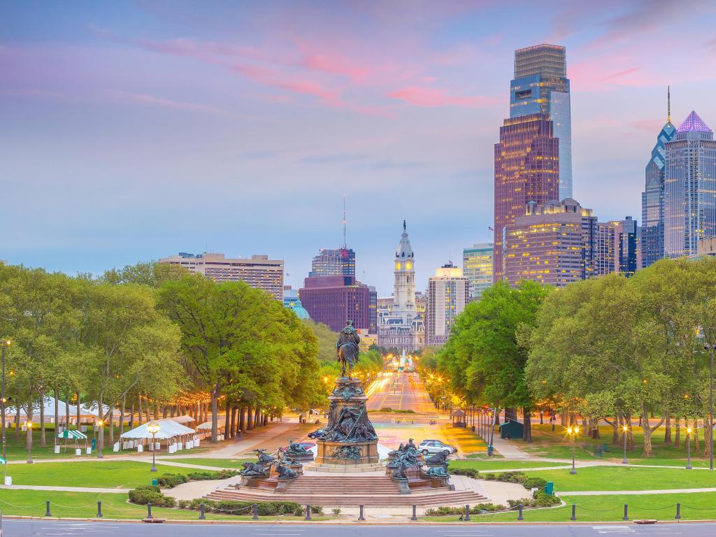 Philadelphia in Pennsylvania, USA with the cityscape of downtown skyline in the background and a green park and monument in the foreground taken at sunset.