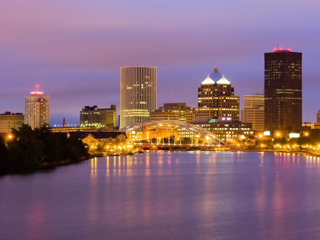 Rochester, New York State, USA taken at night with pink hues in the sky, the sea in the foreground and the city skyline in the background.