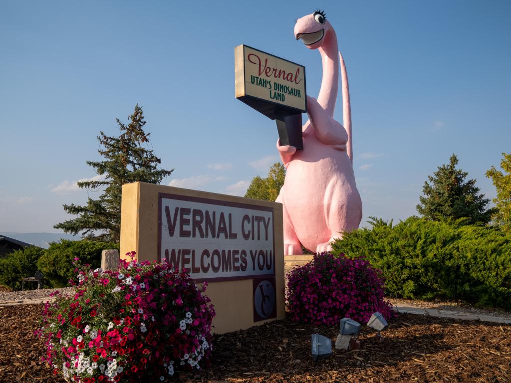 Vernal's pink dinosaur statue holding up a welcome sign on a sunny day