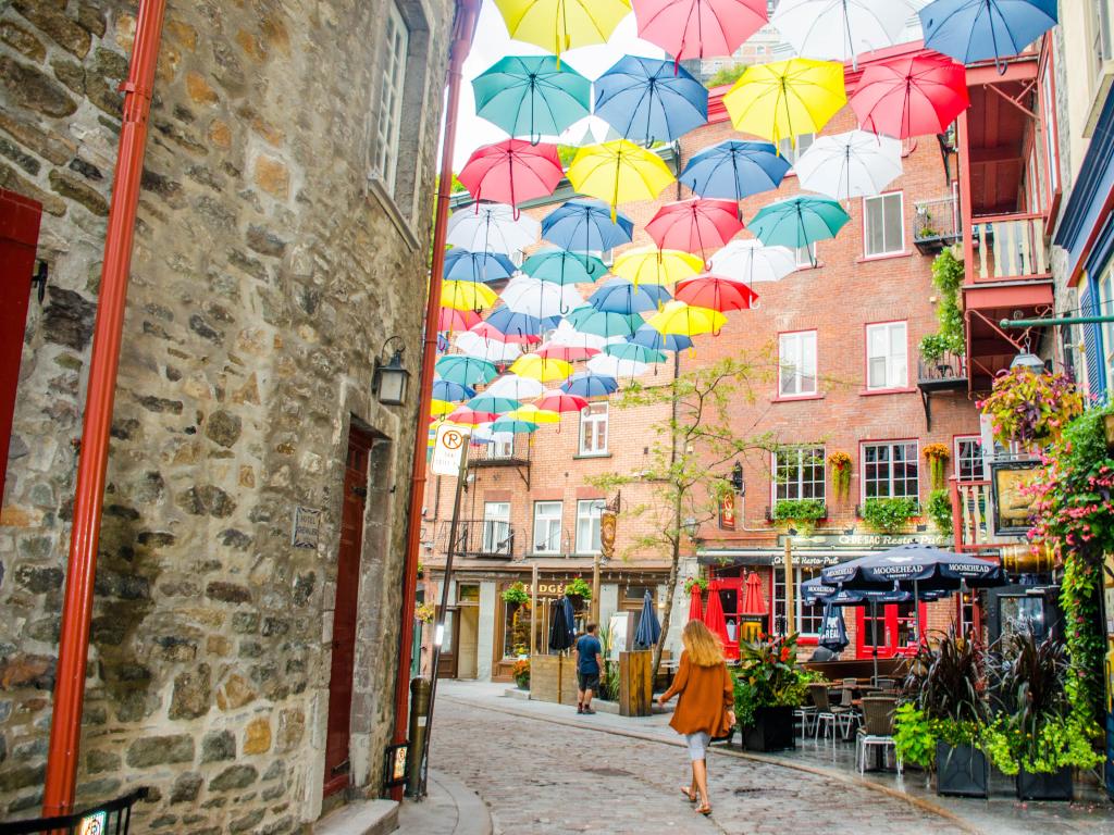 Quebec City, Canada showing a corner of a street with tables and chairs outside a restaurant and different coloured umbrellas hanging from the tops of buildings.