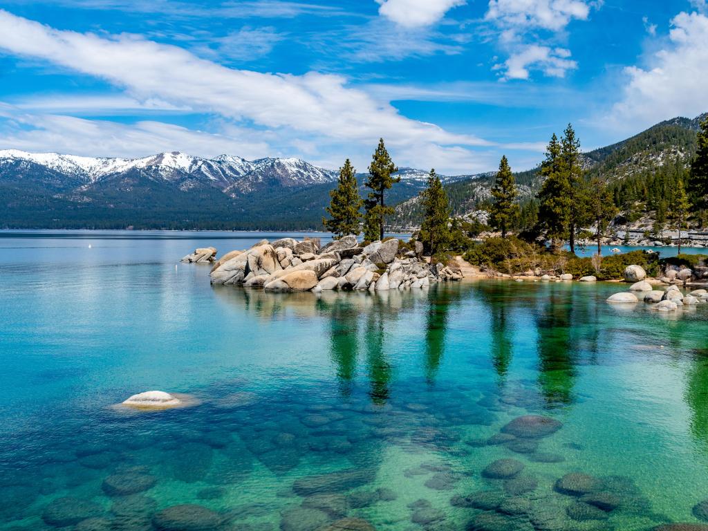 Crystal clear waters of Lake Tahoe surrounded by thin tall trees and mountain peaks
